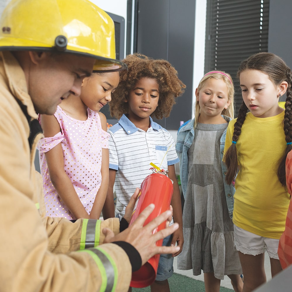 Firefighter teaching fire extinguisher safety to students in a classroom.