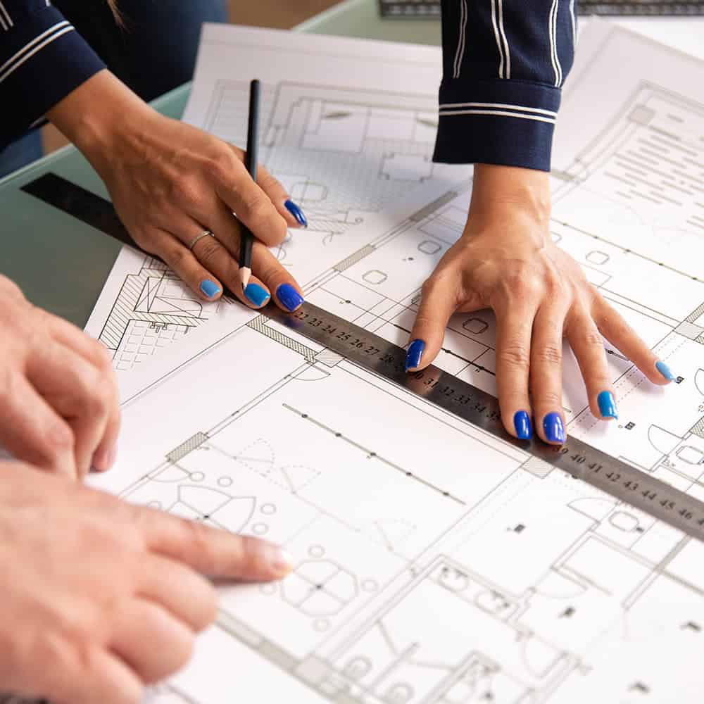 Close-up of architects' hands using a ruler and pencil to analyse a CAD-generated house plan.